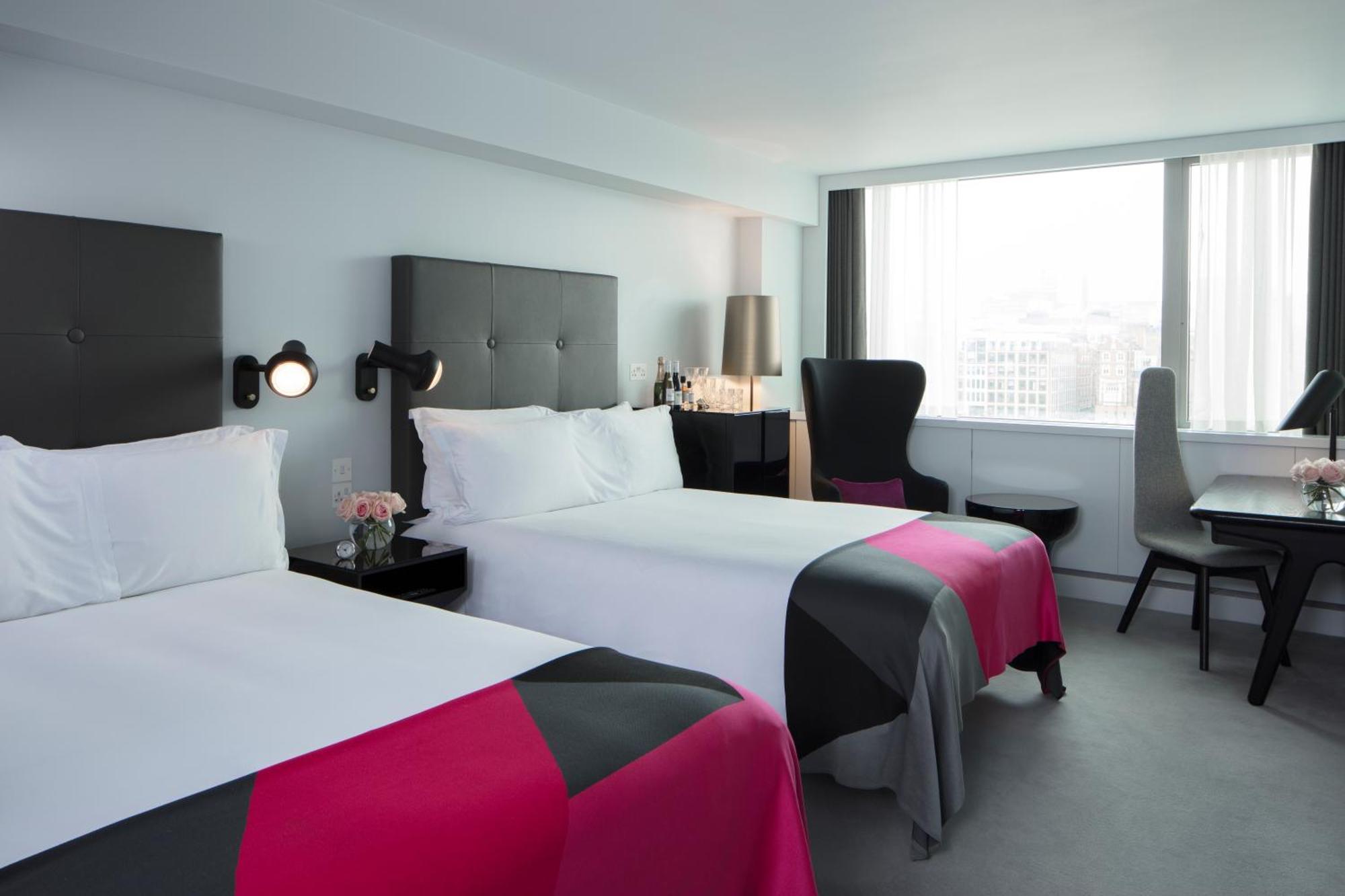 Готель Sea Containers Лондон Екстер'єр фото The photo shows a modern hotel room featuring two beds, each with white linens and colorful throws in shades of pink and gray. The room has a contemporary design, with dark upholstered headboards and stylish wall lamps beside each bed. There is a sma