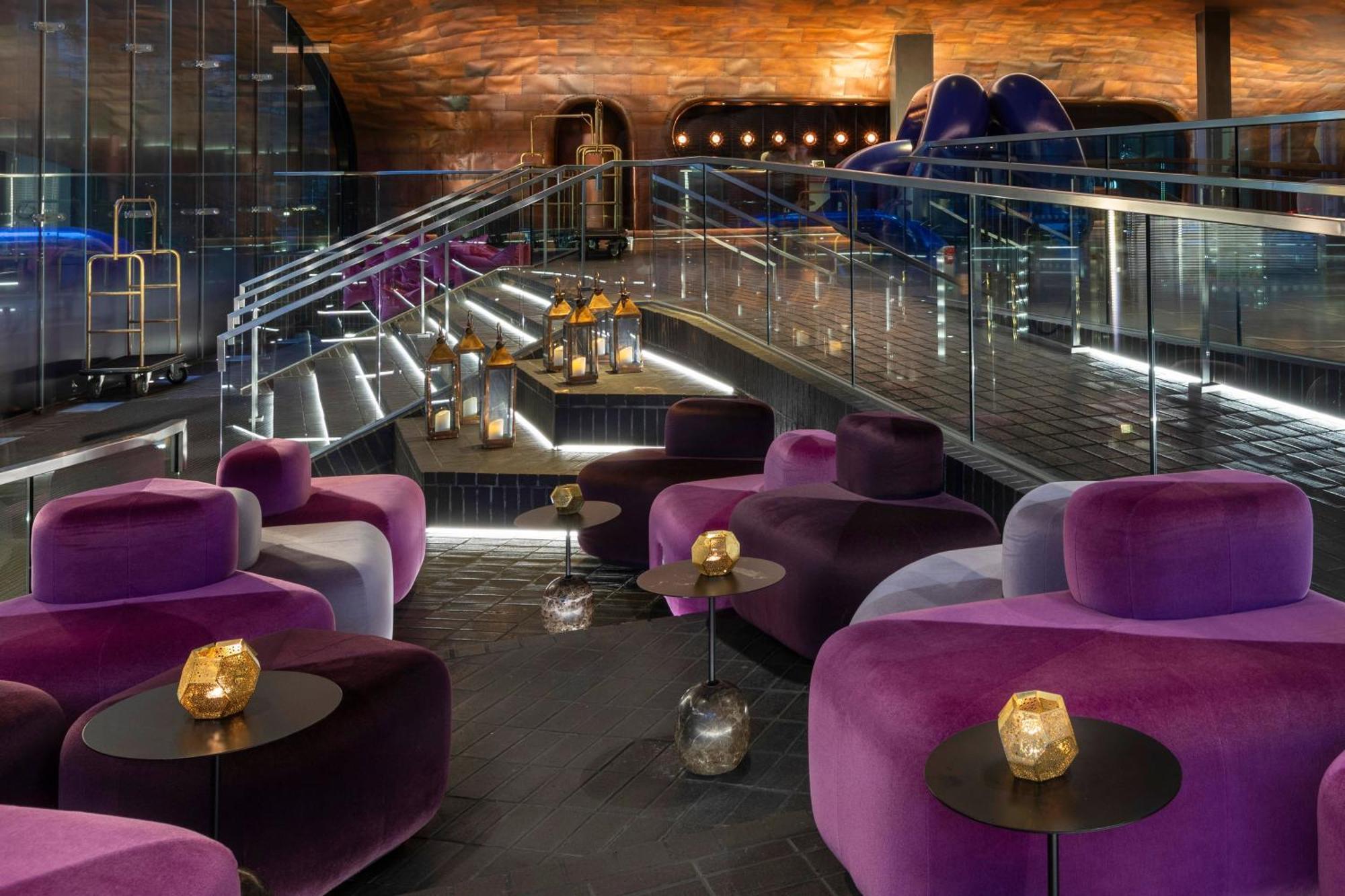 Готель Sea Containers Лондон Екстер'єр фото The photo depicts a stylish interior space, likely a lounge or bar. It features modern, plush seating in shades of purple and velvet textures, arranged around small tables that hold decorative candle holders. The lighting is ambient, highlighting the