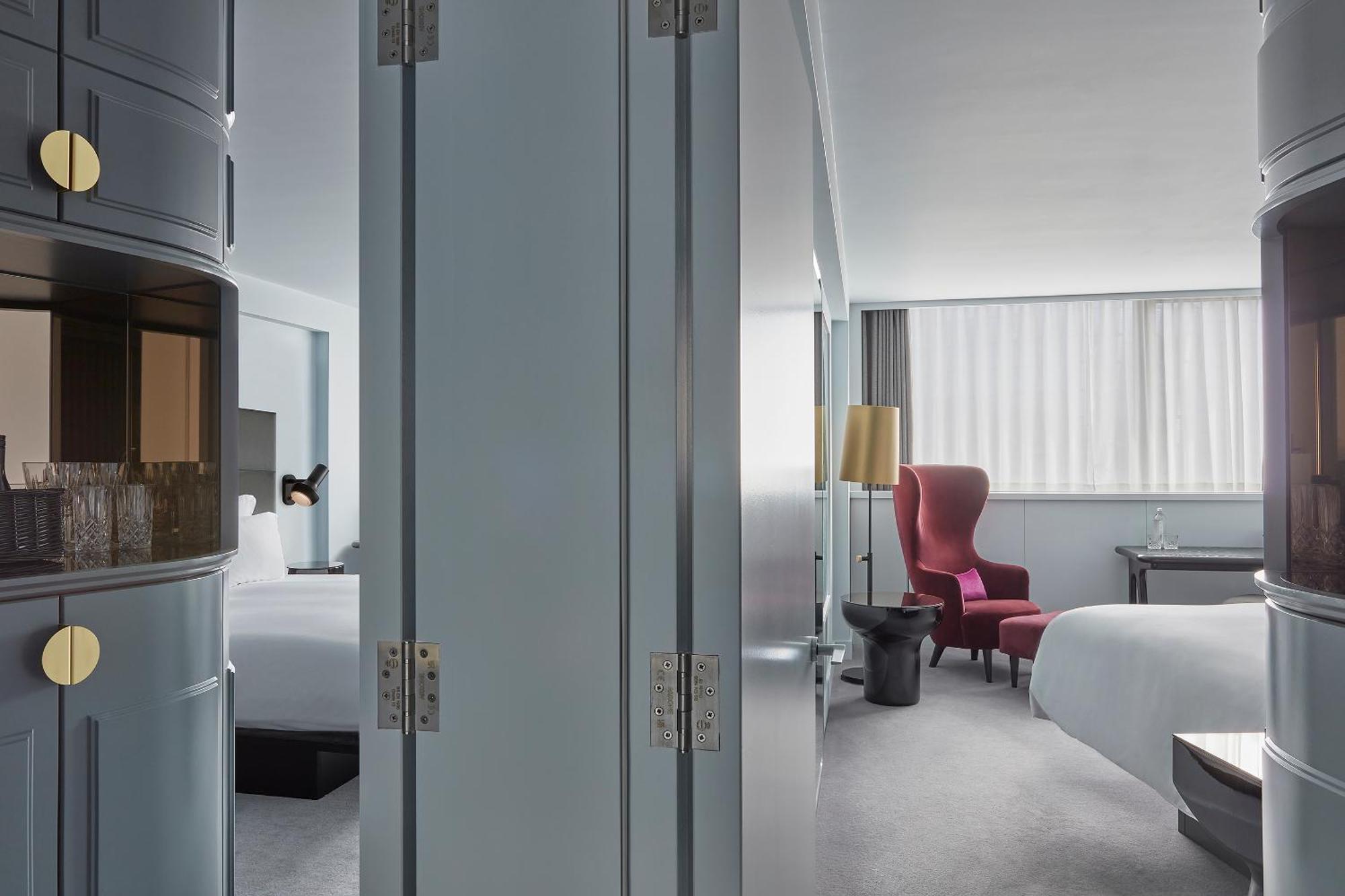 Готель Sea Containers Лондон Екстер'єр фото The photo shows an interior space that appears to be a modern hotel room. The room is divided by a pair of large, grey doors that are slightly ajar. To one side, there are elements that hint at a welcoming, spacious ambiance, such as a bed with white