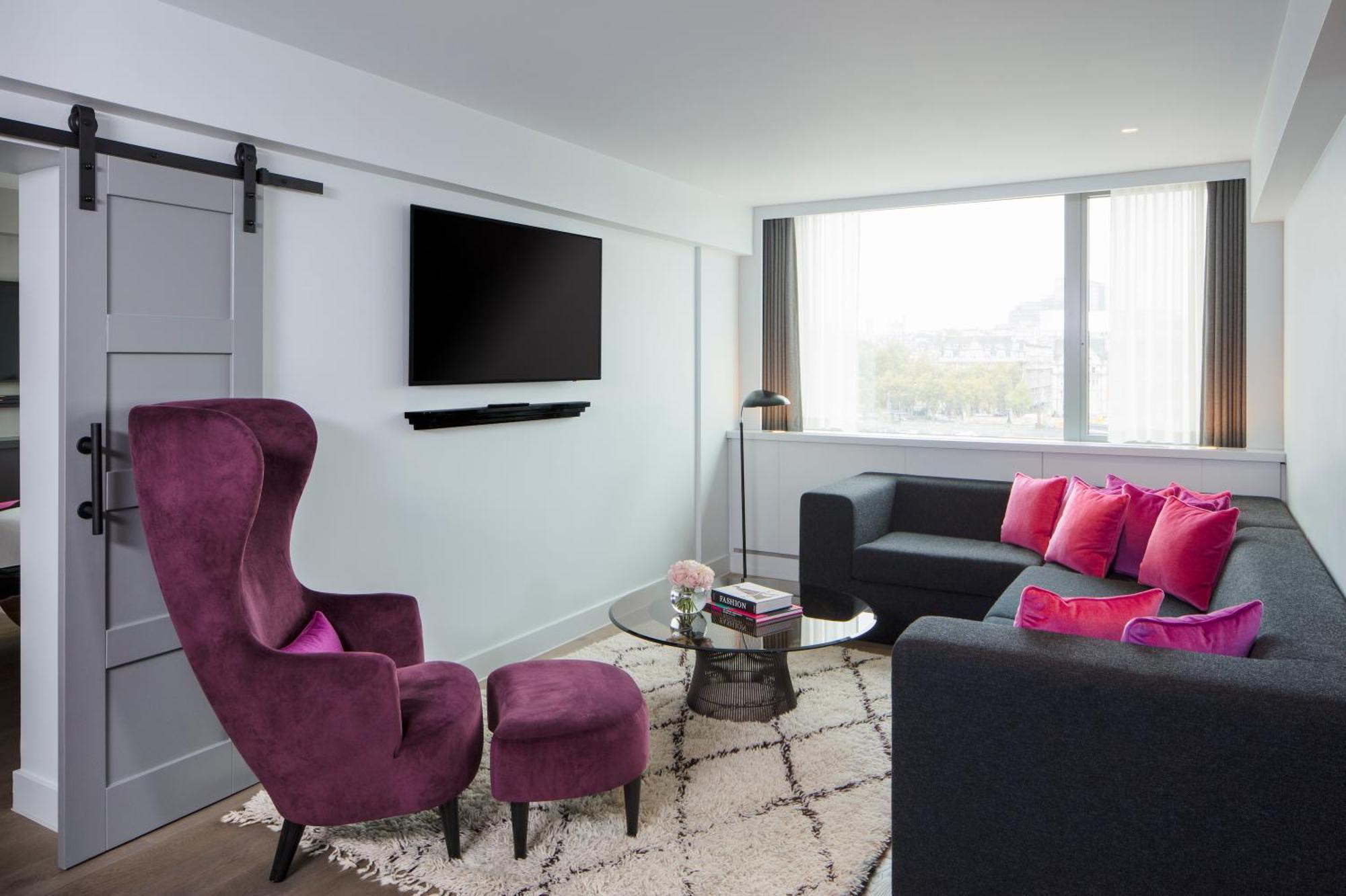 Готель Sea Containers Лондон Екстер'єр фото The photo shows a modern living room with a clean and stylish design. There is a large window that allows natural light to fill the space. A comfortable dark sofa is accompanied by vibrant pink cushions, adding a pop of color. Next to the sofa is a r