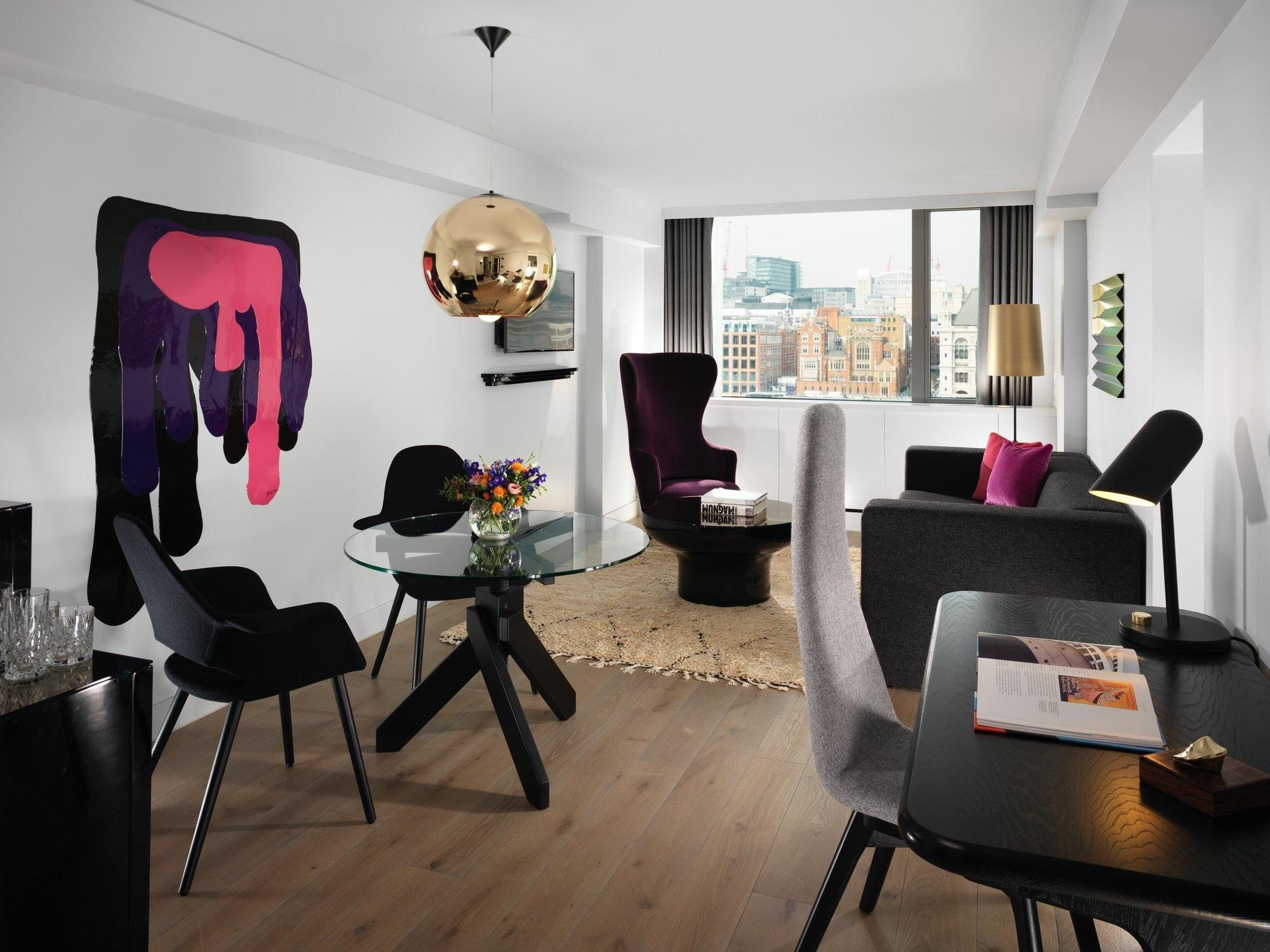 Готель Sea Containers Лондон Екстер'єр фото The photo shows a modern and stylish living space. It features a light-colored wooden floor and a layout that includes a glass dining table surrounded by black chairs. There’s a lounge area with a couple of armchairs, one of which has a playful and u