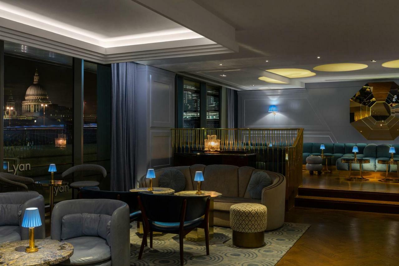 Готель Sea Containers Лондон Екстер'єр фото The photo depicts a stylish interior of a lounge or bar. The space features elegant seating arrangements, including plush sofas and chairs, with small tables placed throughout. Ambient lighting is provided by small blue lamps on the tables and recess